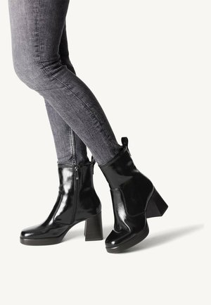 Sorte patentlæder ankelstøvler med en kraftig hæl, sidelukning og en glat, skinnende overflade. Kombineret med mørkegrå skinny jeans.