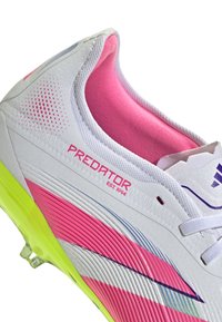 Witte voetbalschoenen met roze en gele accenten, voorzien van een gestructureerd oppervlak, ribbelontwerp en 'Predator' branding in het roze.
