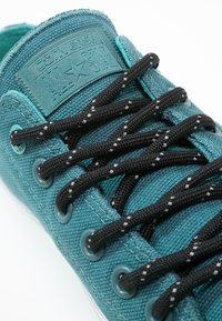 Baskets en toile bleu sarcelle avec un profil bas, des lacets noirs et des œillets circulaires. Caractérisées par une languette texturée avec un logo. Semelle en caoutchouc visible.