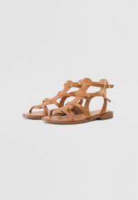 Sandales en cuir tan avec plusieurs lanières croisées et une boucle à la cheville. Semelle plate avec une surface texturée et un design minimaliste.