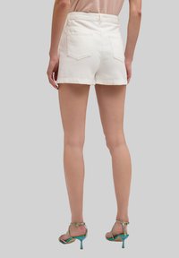Witte denim short met een hoge taille, achterzakken en een rafelige zoom. Draagt een kleurrijke strappy hoge hakken.