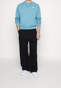 Světle modrá mikina s kulatým výstřihem a bílým logem Nike, doplněná černými kalhotami s širokými nohavicemi a bílými teniskami. Jednoduchý, nenáročný outfit.