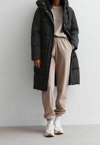 Pitkä musta toppatakki hupulla, yhdistetty beigen värisiin verkkareihin ja valkoisiin tennareihin. Takissa on tikattu kuviointi ja joustavat hihansuut.