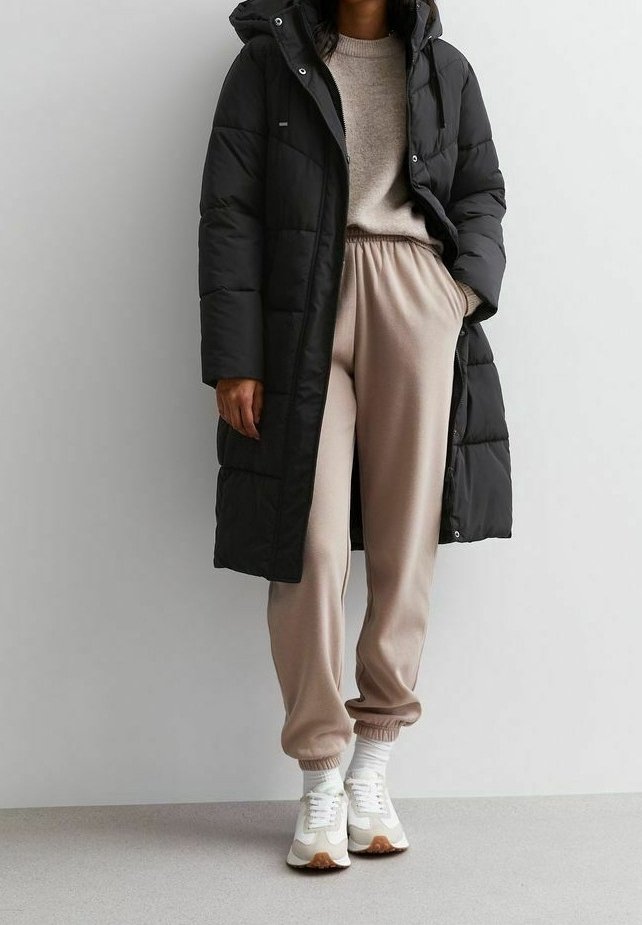 Pitkä musta toppatakki hupulla, yhdistetty beigen värisiin verkkareihin ja valkoisiin tennareihin. Takissa on tikattu kuviointi ja joustavat hihansuut.