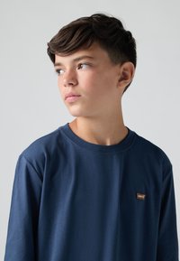 Sötétkék hosszú ujjú póló, pamutból készült, kerek nyakkivágással és apró barna Levi's logóval a mellrészen. Sima textúra.