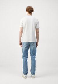 Hvit bomull t-skjorte med korte ermer, kombinert med lyseblå denimbukser. Avslappet passform, med subtil søm og baklommer synlige.