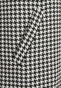 Tissu à motif pied-de-poule noir et blanc avec une texture lisse. Comprend une boucle ou un onglet rectangulaire en tissu en guise d'accent.