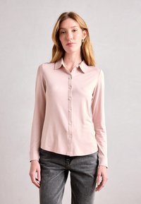 Langermet, lys pink bluse med knappestolpe foran og krage. Mykt stoff med en jevn tekstur. Kombinert med grå jeans.