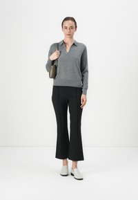 Pullover grigio lavorato a maglia con scollatura a V e maniche lunghe, abbinato a pantaloni neri a fantasia e scarpe slip-on di colore chiaro. Accessorio borsa di piccole dimensioni.