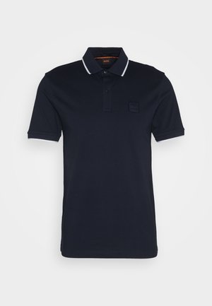 Tumesinine polo särk klassikalise kraega, kahe nupuga kinnitusega, valged aktsendid varrukatel ning tekstureeritud logopatch vasakul rinnal.