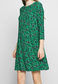 Green dress in floral pattern with black accents, round neckline, and three-quarter sleeves. Made from lightweight fabric, A-line shape.