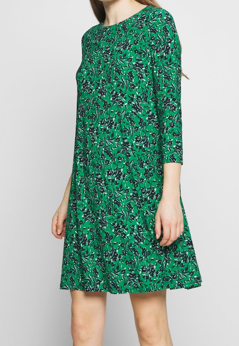 Green dress in floral pattern with black accents, round neckline, and three-quarter sleeves. Made from lightweight fabric, A-line shape.