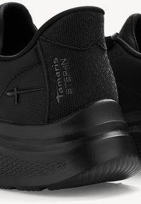 Melnas sporta kurpes ir aprīkotas ar teksturētu virsmu, mīkstu apkakli un biezu, atbalstošu zoli ar rakstainu protektoru. Zīmols ir izspiedēts sānos.