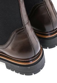 Gros plan de bottes en cuir marron avec panneaux latéraux élastiques noirs et semelles épaisses en caoutchouc noir avec une bordure beige.