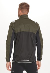 Giacca sportiva da uomo con colletto zip, pannello superiore verde oliva, sezione inferiore nera e dettagli riflettenti sulle spalle e sulla schiena.