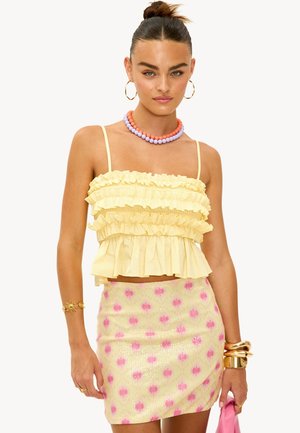 Top court froncé jaune avec de fines bretelles, associé à une mini-jupe à sequins rose et jaune avec un motif floral. Les accessoires comprennent un collier en perles colorées.