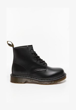 Zwarte leren veterschoen met enkellengte, ronde neus, dikke zool, gestikte accenten en een gele trekband aan de achterkant. Gladde textuur.