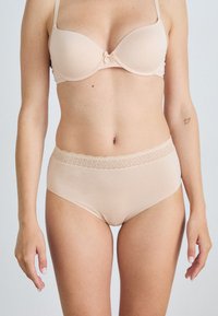 Beige bh og høyhøyde undertøy sett, laget av glatt stoff. Underdelen har en blondekant i livet for detalj.