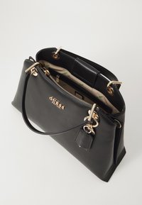 Borsa a mano in pelle nera con design strutturato, hardware color oro, zip in cima e un piccolo tag accessorio attaccato.
