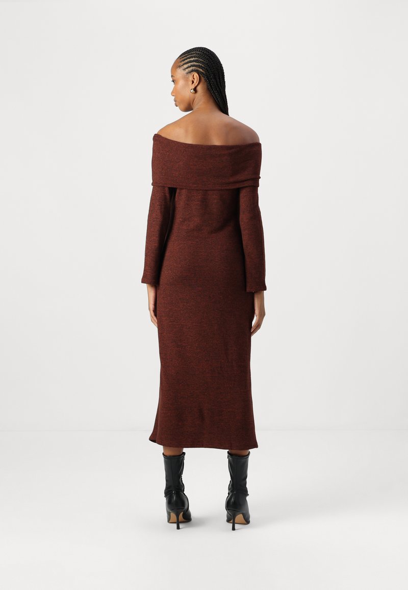 Vestido rojo oscuro, de manga larga y hombros al aire, en un tejido de punto texturizado, de longitud a media pantorrilla, combinado con botas negras de cuero de punta.