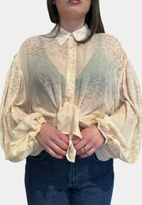 Blusa leggera e trasparente color crema con una sottile stampa animale beige, maniche a palloncino oversize, chiusura con bottoni e dettaglio annodato in vita.