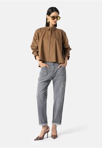 Smeđa skraćena košulja, sivi široki traperice s istrošenim detaljima i cipele s uzorkom leoparda s visokom petom. Prevelike sunčane naočale upotpunjuju izgled.