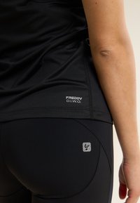 Top atlético negro con un logotipo en el dobladillo, combinado con leggings negros que presentan un pequeño logotipo reflectante cerca de la cintura. Textura suave.