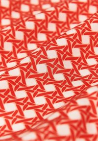 Tissu blanc avec un motif répétitif de formes géométriques rouges interconnectées formant des motifs circulaires.