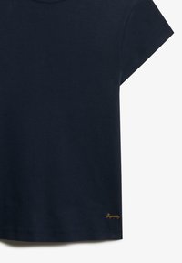 Marineblauwe katoenen t-shirt met een ronde hals, korte mouwen en een klein goud geborduurd logo aan de onderrand. Gladde textuur.