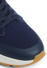 Zapatilla deportiva azul marino con parte superior de malla texturizada, puntera suave y suela de goma con un acento marrón claro. Presenta cordones planos.