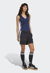 Navy sleeveless sports top with white side stripes, paired with black shorts featuring white accents. Black socks with three white stripes and shoes.