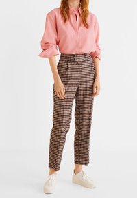 Lichtroze blouse met knopen en oprollende mouwen, gecombineerd met hoog-waist geruite broeken in rood, zwart en wit, gedragen met witte sneakers.