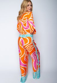Farbiger Outfit mit einem Langarm-Oberteil und weit geschnittenen Hosen. Hergestellt aus glattem Stoff mit abstrakten Mustern in Orange, Pink und Türkis.