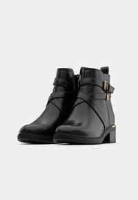 Čierne členkové čižmy vyrobené z hladkej kože s dekoračnými prúžkami a zlatým kovovým sponou. Mierne štruktúrovaný podpätok s gumovou podrážkou.