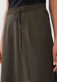 Oliivinvihreä, kevyt hame, joka on valmistettu pehmeästä kankaasta. Siinä on joustava vyötärönauha nyörillä ja sivuhalkio.