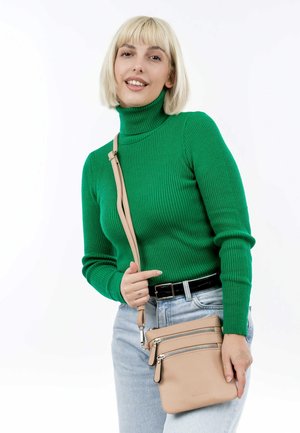 Pull à col roulé côtelé vert, jeans bleu clair et sac bandoulière en cuir beige avec trois compartiments zippés, accents en métal argenté.