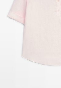 Chemise rose clair à manches courtes avec col henley et trois boutons, avec un ourlet droit et des manches simples à revers.