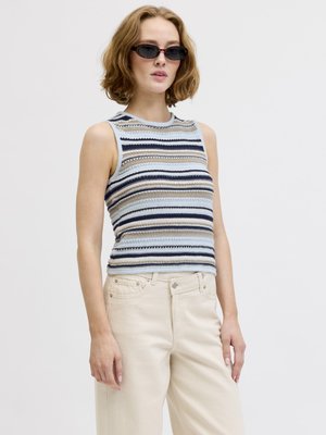 Mujer con gafas de sol negras de estilo cat-eye, un top de punto sin mangas con rayas en azul, beige y blanco, y pantalones de talle alto color blanco roto.