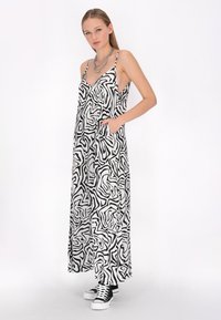 Rochie maxi cu un model alb-negru, cu bretele subțiri, decolteu în V, buzunare laterale și o siluetă lejeră, combinată cu adidași alb-negru.