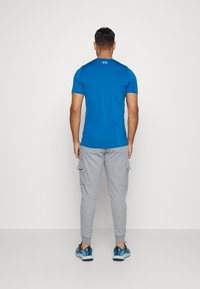 Aktivitetsklær med en blå t-skjorte med korte ermer og grå cargo-bukser. Materialet ser lett ut; t-skjorten har en tettsittende design, og cargo-buksene har sidelommer.