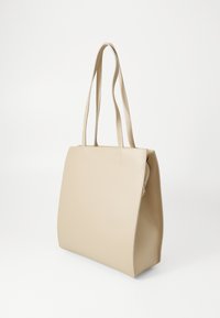 Beige tote bag med glatt lærtekstur, rektangulær form og lange doble håndtak. Har en glidelås og rene sømmer som detaljer.