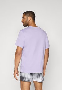 Lavender short-sleeve t-shirt made of cotton, featuring a classic crew neckline and a plain back design, paired with gray tie-dye shorts.