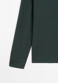 Dunkelgrünes Langarmshirt mit strukturierter Stoffqualität, gekrempelten Ärmeln und geradem Saum. Das Material wirkt atmungsaktiv und weich.