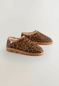 Zapatos marrones tipo slip-on con un patrón de estampado de leopardo, que cuentan con un forro suave, suela de goma y un detalle de costura mínima.