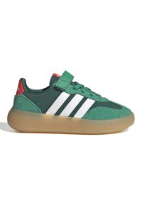Green sneaker with white stripes, gum sole, red heel tab, laces, and a green Velcro strap across the top.