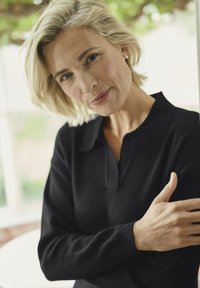 Polo-shirt noir à manches longues avec col et poignets côtelés, fabriqué en matériau doux. Gros plan sur une personne montrant une posture détendue.