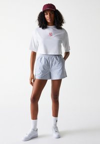 White cropped t-shirt with red logo, blue and white striped shorts, maroon cap, white sneakers, and white crew socks. Casual outfit.