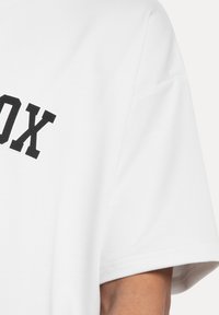 Weißes Rundhals-T-Shirt aus Baumwolle mit kurzen Ärmeln und einem großen schwarzen Druck des Wortes "BOX" auf der Vorderseite.