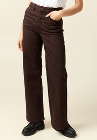 Bruna vida byxor med ett leopardsmönster, tillverkade av kraftigt tyg. Har framfickor och en knäppt midja. Svarta stövlar synliga.