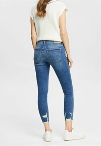 Smala blå jeans i denim, med en blekt finish, slitna fållar och två bakfickor. Kombinerat med en vit tröja och sneakers.